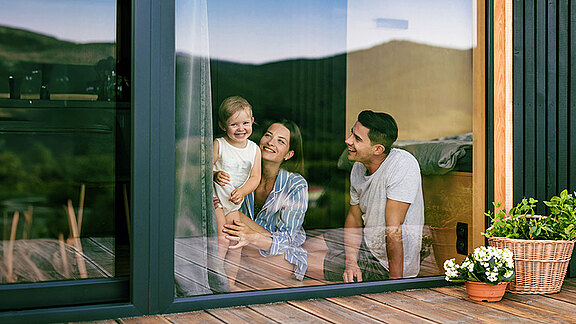 Junge Familie genießt den Blick aus ihrem Einfamilienhaus ins Freie.